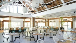 Un restaurant spacieux doté de hauts plafonds, bénéficiant d’une lumière naturelle et offrant différents types d’aménagements, notamment des tables et des chaises.
