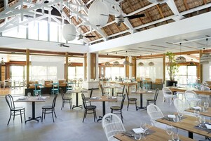A spacious restaurant with high ceilings, natural light, and a variety of seating arrangements including tables and chairs.