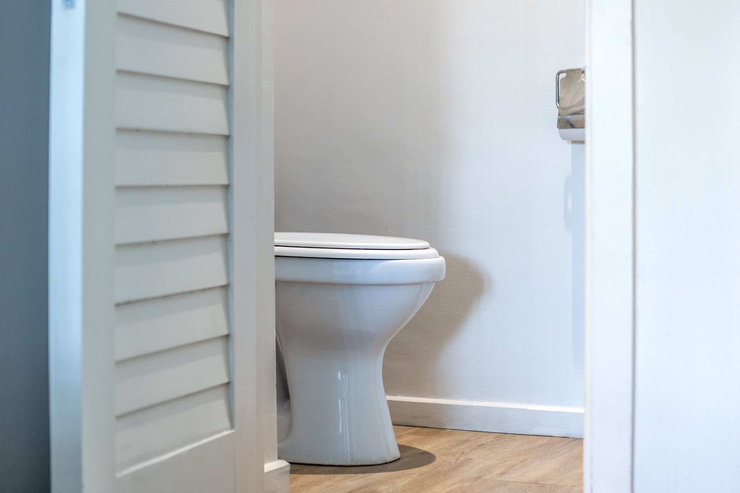 A white toilet in a bathroom with wooden flooring and a white door with a silver handle.
