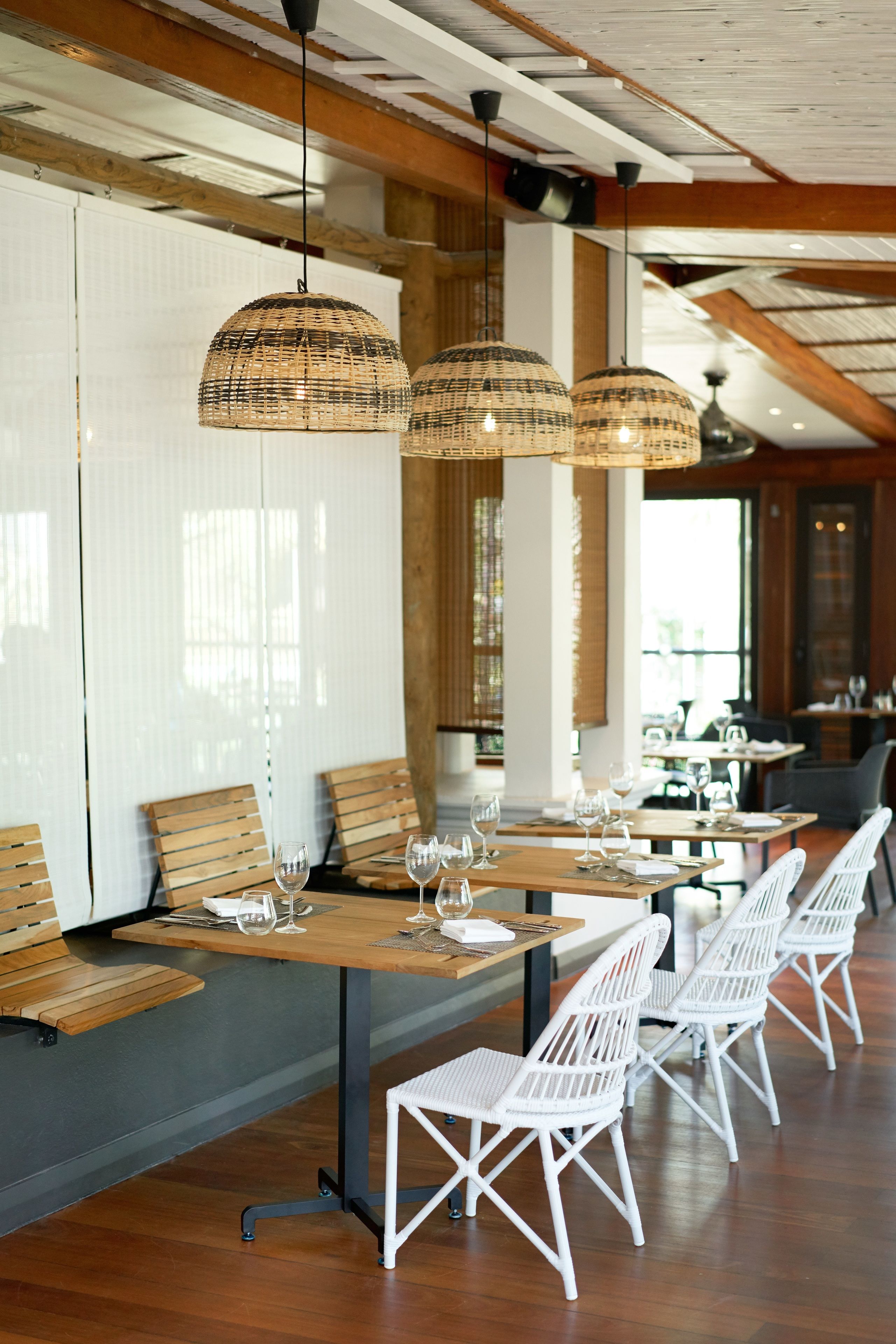 Un ristorante con tavoli di legno e sedie bianche, lampadari in vimini appesi e vista sulla sala da pranzo.