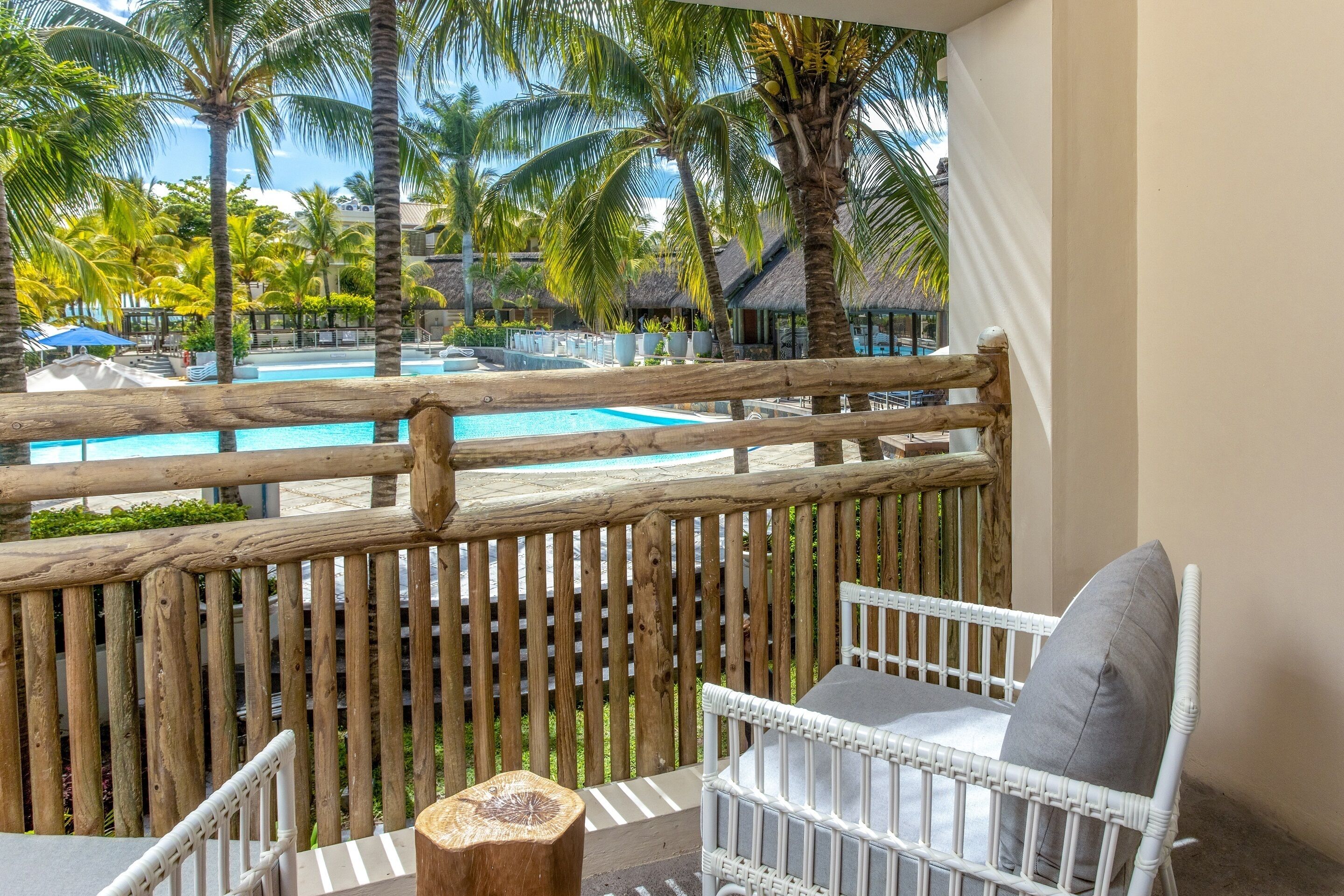 Un balcón con vista a una piscina, rodeado de palmeras y una cerca de madera.