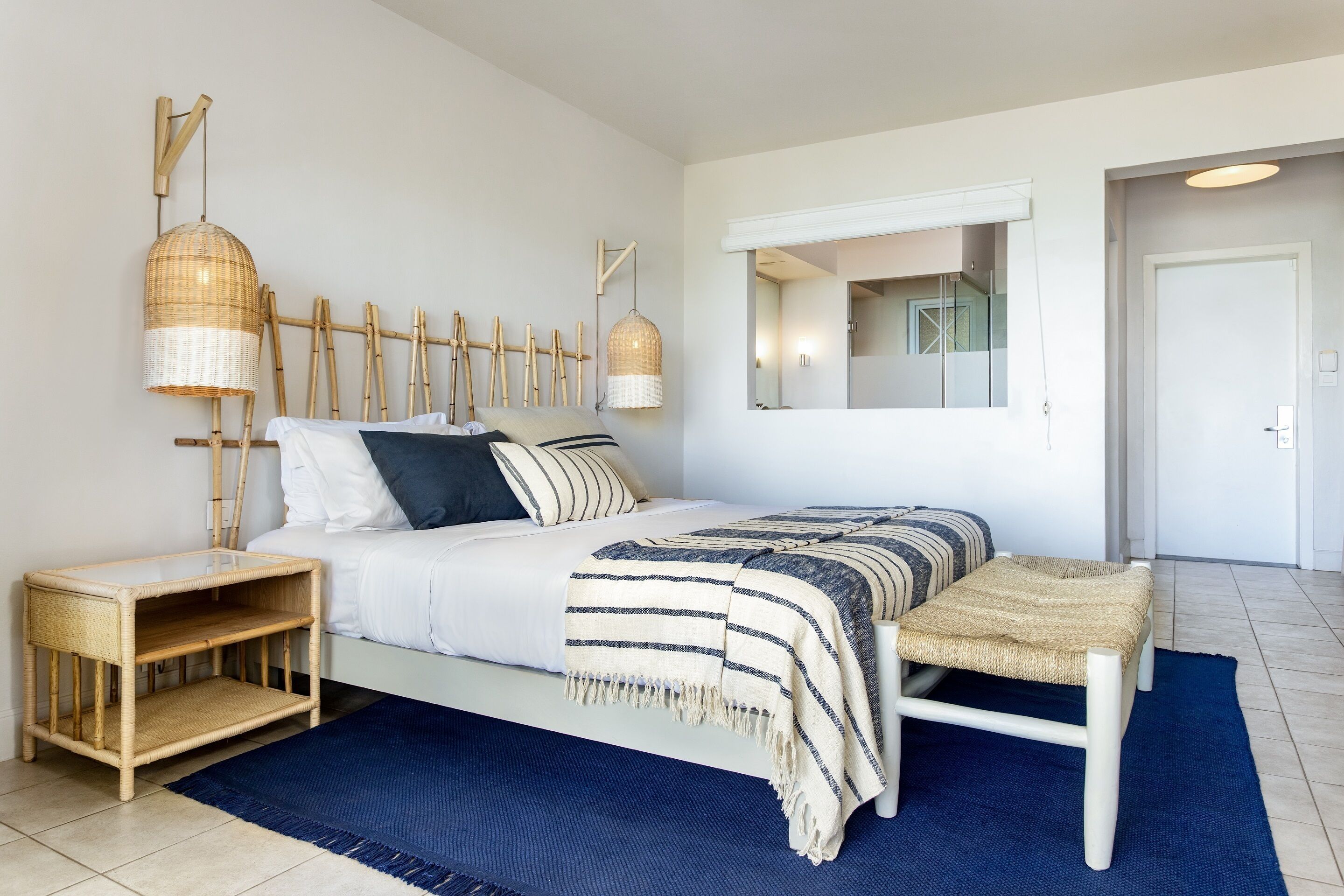 A bedroom with a bed, bedside tables, a mirror, and a blue rug.