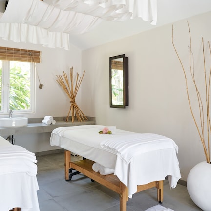 A spa room with two treatment beds, a large window, a sink, and a mirror.