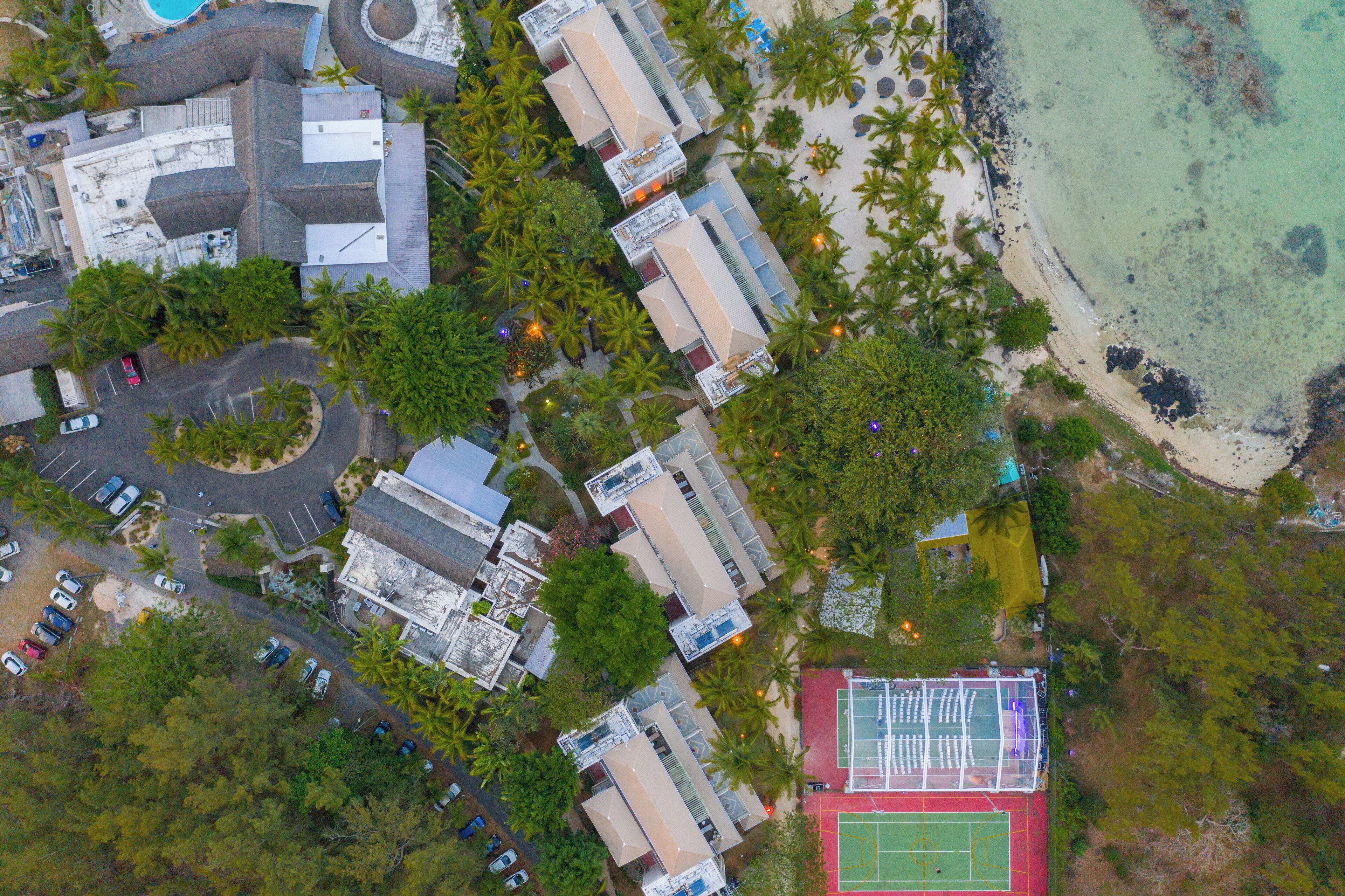 Vista aérea de un complejo turístico con varias edificaciones, una playa y una cancha de tenis.