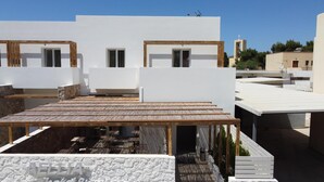 Une terrasse sur le toit, dotée d’un plancher en bois et d’un mur en pierre, sur laquelle on peut voir une enseigne indiquant « HÔTEL AELLA ».