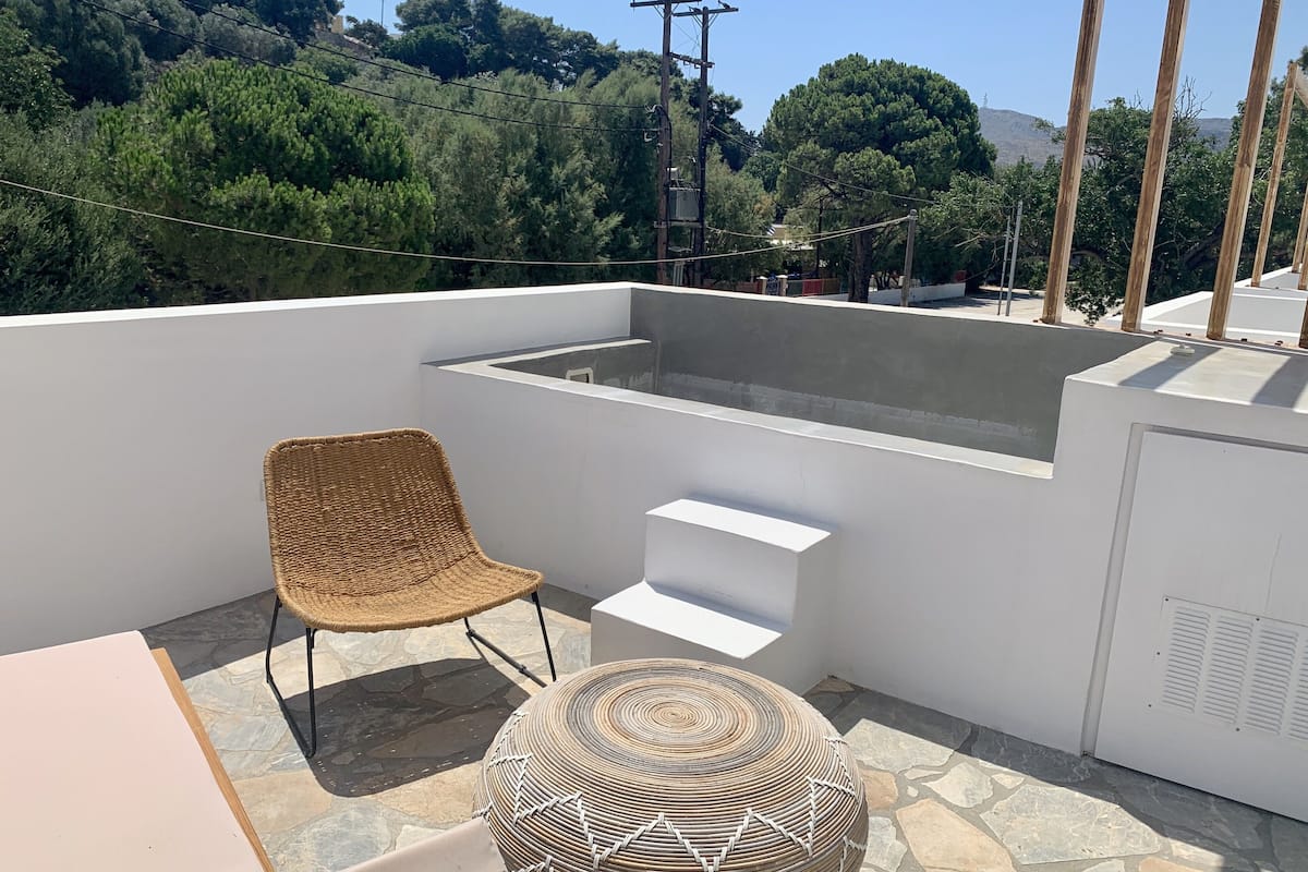 Terraza en la azotea con una silla de mimbre, un taburete redondo tejido y un banco blanco.