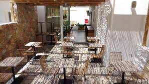 An outdoor seating area with wicker chairs and tables, stone walls, and a view of the garden. - Aellia Hotel & Suites (Leros)