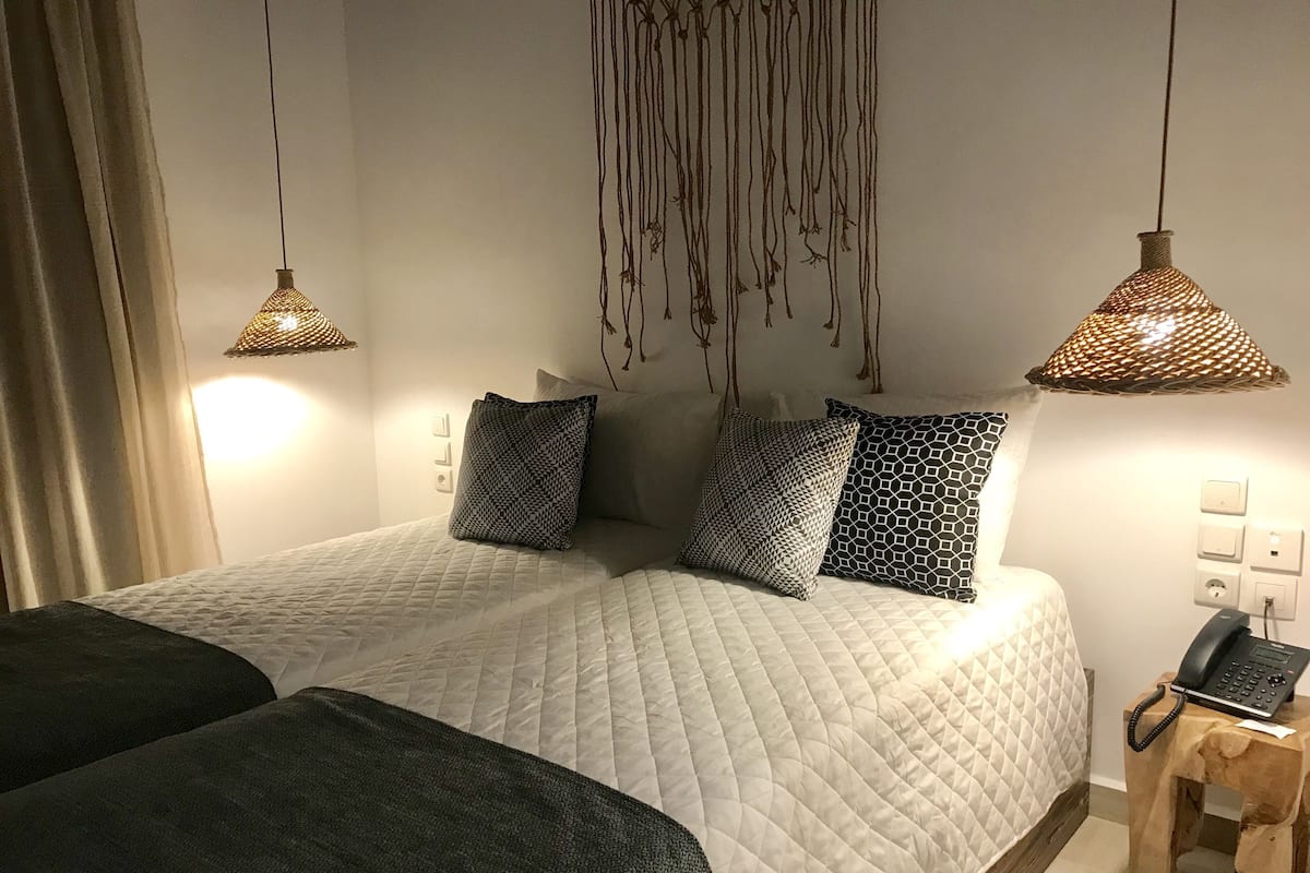 Una cama doble con edredón blanco acolchado, dos almohadas estampadas y una mesita de noche con un teléfono.