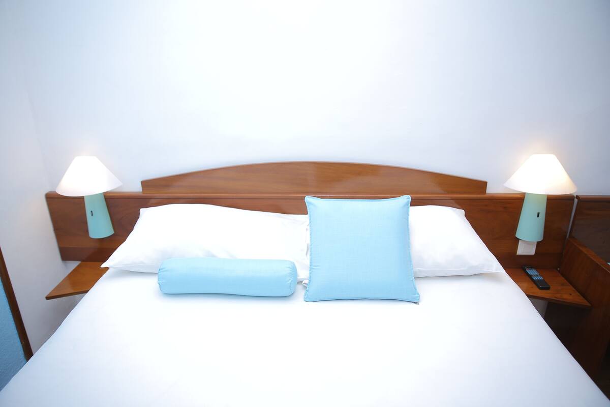 A neatly made bed with white and light blue pillows, wooden headboard, and bedside lamps.