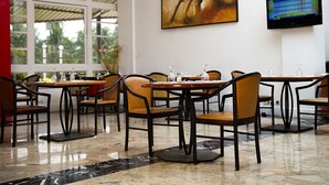 Un restaurante con una decoración moderna, que presenta un cuadro grande en la pared, un televisor de pantalla plana y un comedor con mesas y sillas.