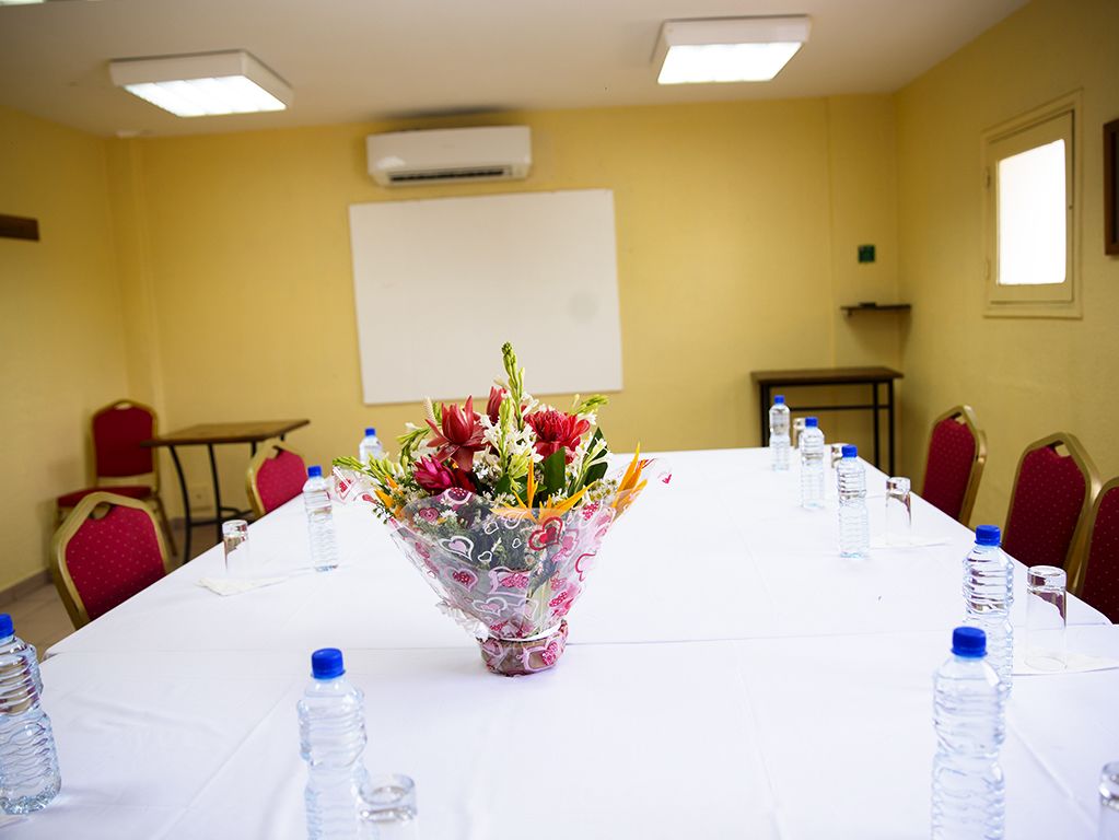 A conference room with a long table, floral centerpiece, water bottles, and red chairs.