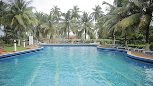 Una piscina con palmeras, sillas de descanso y una sombrilla roja.