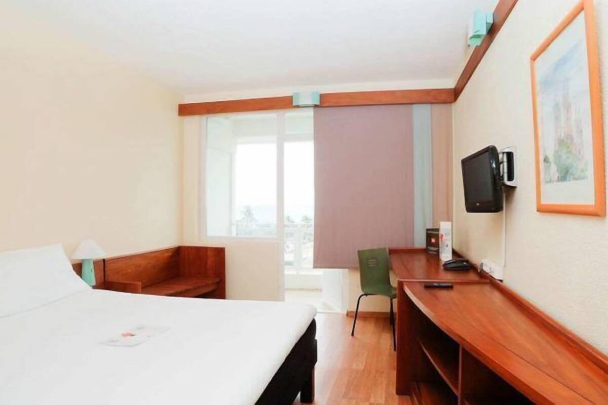 A hotel room with a bed, a desk, a chair, a television, and a window.
