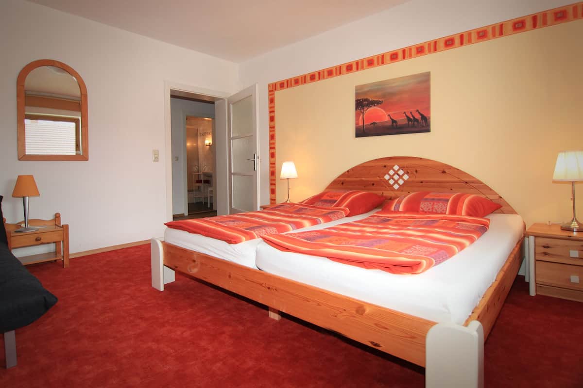 A bedroom with a wooden bed, a red carpet, a mirror, and a painting on the wall.