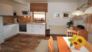 A compact kitchen with white cabinets, a built-in oven, and a window with a view of flowers. - Ferienwohnungen Schmid (Lam)