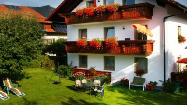 A two-story building with balconies adorned with red flowers, a lawn with chairs, and a mountain in the background. - Ferienwohnungen Schmid (Lam)
