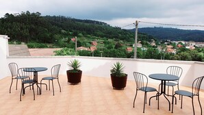 Eine Terrasse mit Sitzgelegenheiten und Pflanzkübeln, mit Blick auf eine Hügelkuppe mit Häusern.