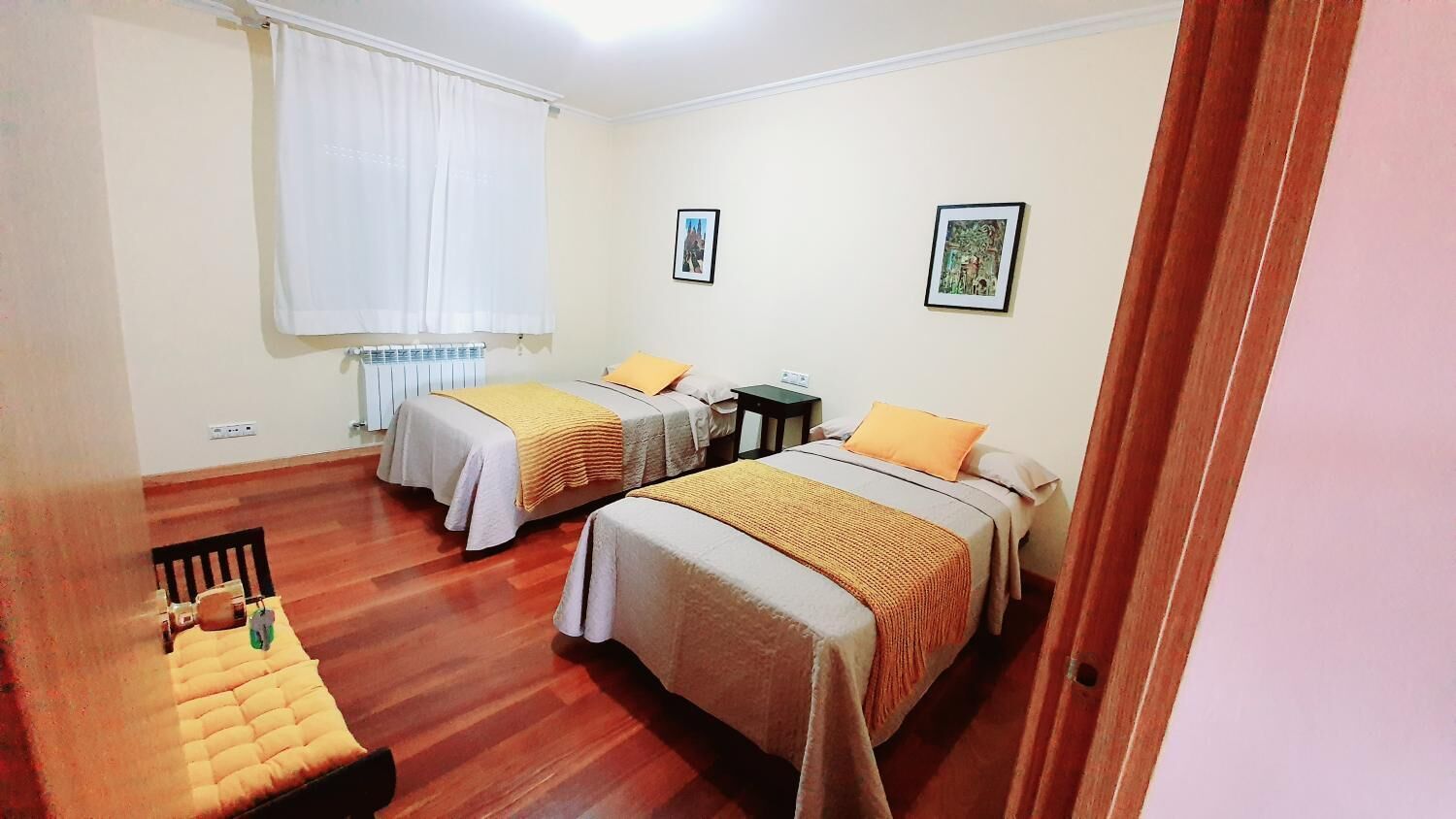 A hotel room with two beds, a wooden floor, a radiator, and two framed pictures on the wall.