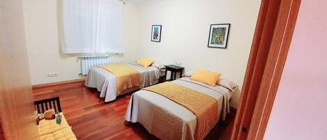 A hotel room with two beds, a wooden floor, a radiator, and two framed pictures on the wall.