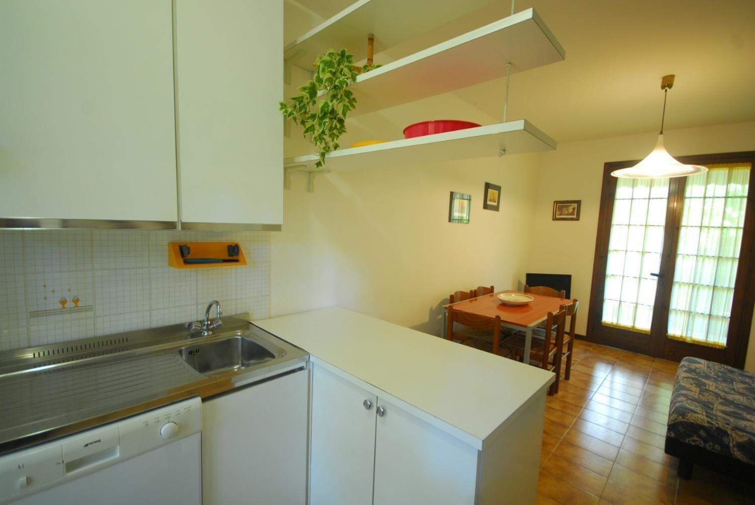 A compact kitchen with a sink, white cabinets, and a dining area with a table and chairs.