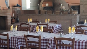 A restaurant with outdoor seating, checkered tablecloths, and a brick oven in the background. - Camping Les Sources (Courthezon)