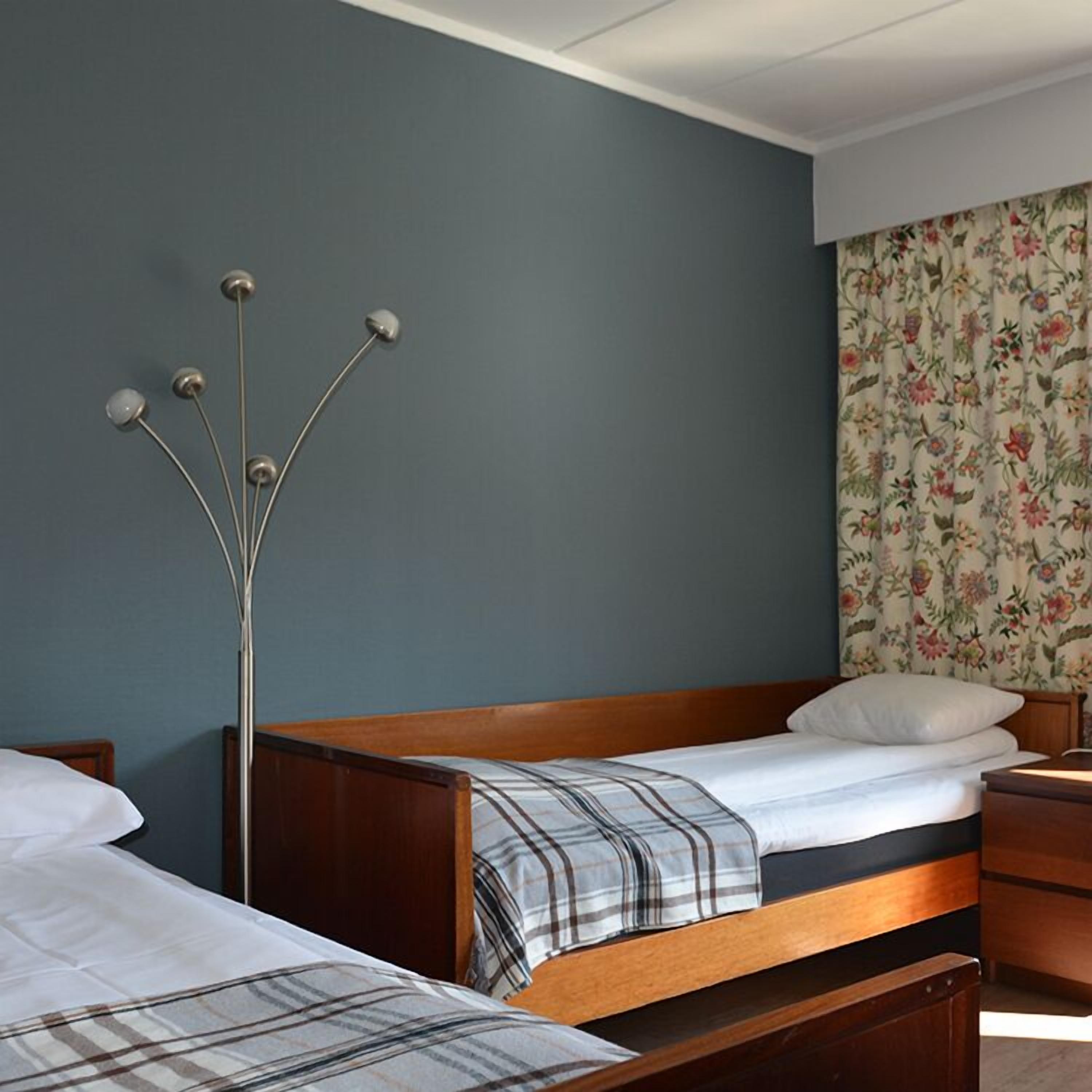 Een slaapkamer met twee houten bedden, een nachtkastje en een hoge vloerlamp.