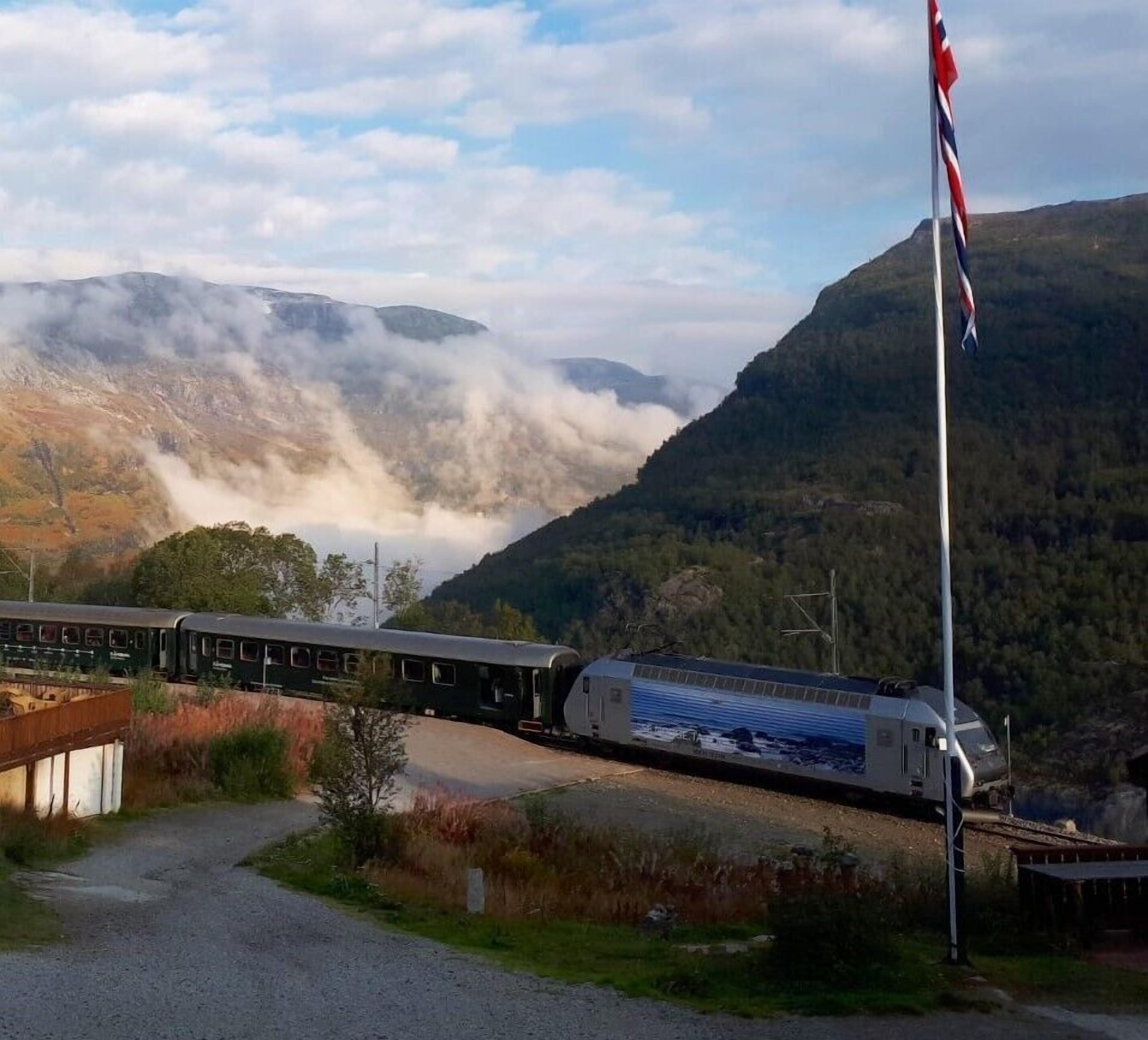 A train passing through a mountainous area with a flag on a pole.
