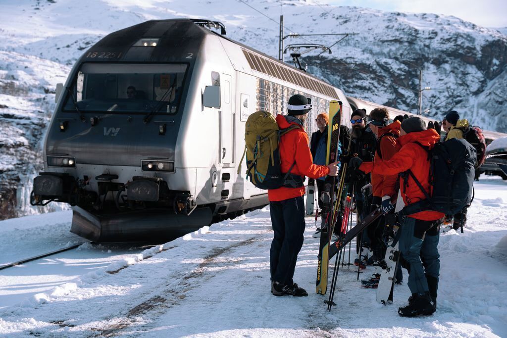 A group of people with skis and snowboards near a train on a snowy path.