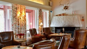 A cozy room with leather chairs, a fireplace, and floral curtains. - Vatnahalsen Høyfjellshotell (Aurland)