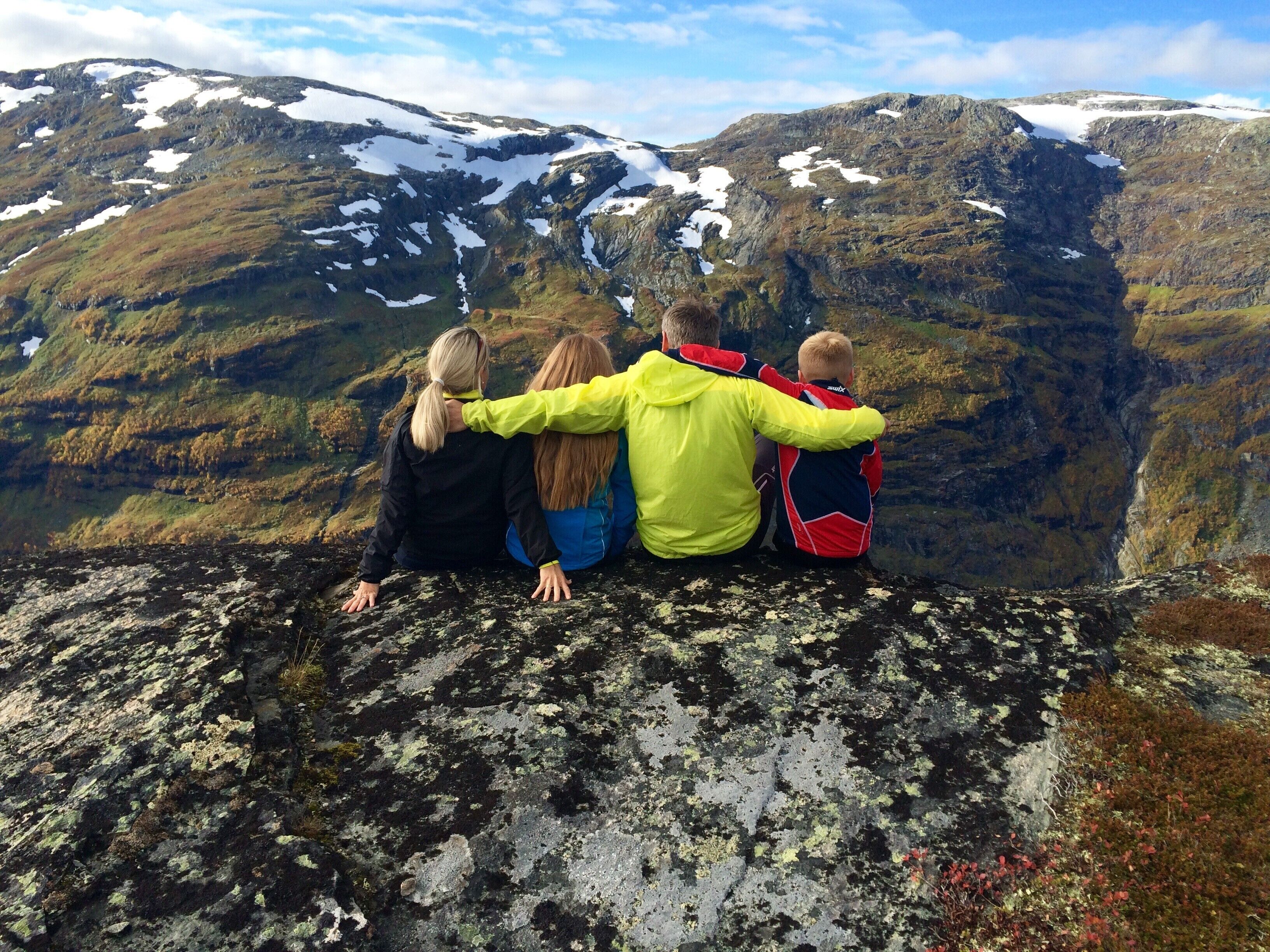 A group of people sitting on a rocky ledge with a mountainous landscape in the background.