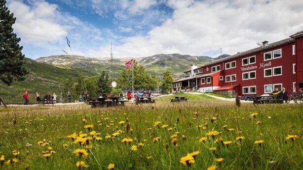 A hotel with a red facade, outdoor seating, and a mountainous backdrop. - Vatnahalsen Høyfjellshotell (Aurland)
