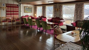 A cozy room with a wooden floor, a red sofa, green chairs, and a wooden table. - Vatnahalsen Høyfjellshotell (Aurland)