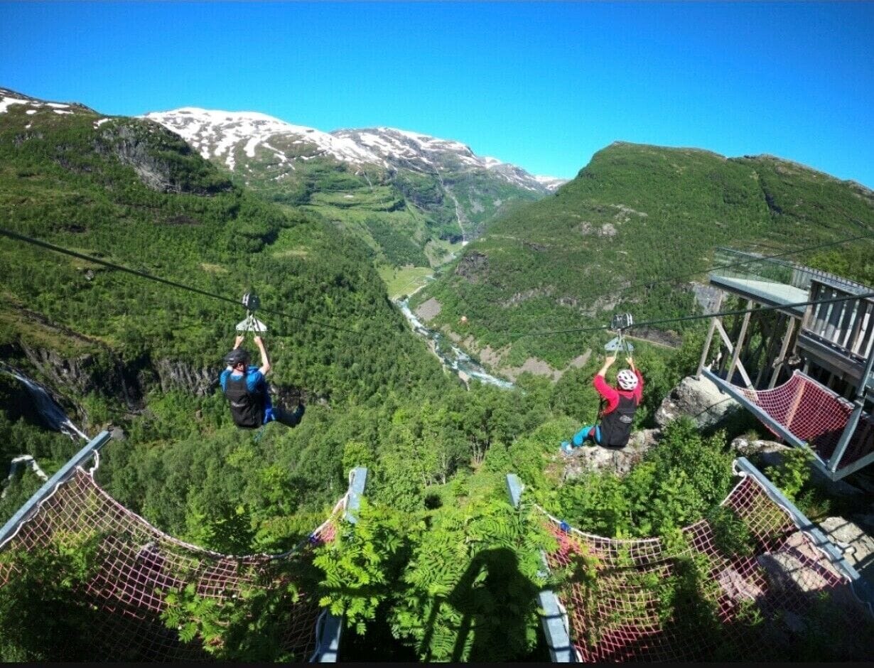 A high-altitude zip-lining course with participants in harnesses, surrounded by lush green forests and a mountain backdrop.