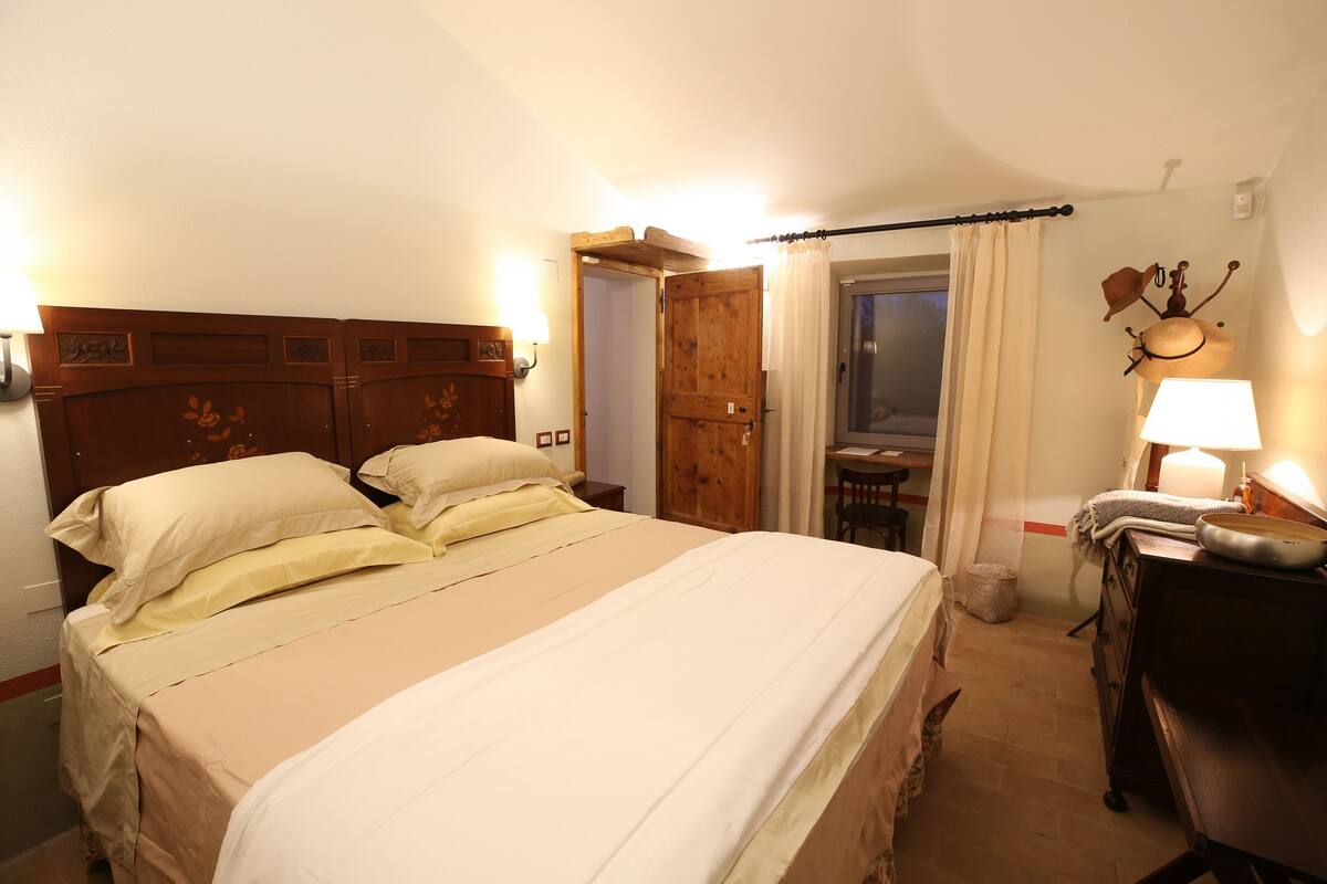 A hotel room with a large bed, wooden headboard, bedside lamps, and a small table with a lamp.