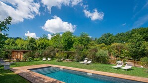 A rectangular swimming pool with a wooden deck, surrounded by a grassy area with several lounge chairs and a wooden pergola. - Casa Minotti (Gubbio)