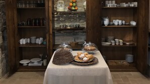 A kitchen with open shelves displaying various dishes and utensils, a central table with a cloth, and a hanging light fixture. - Casa Minotti (Gubbio)