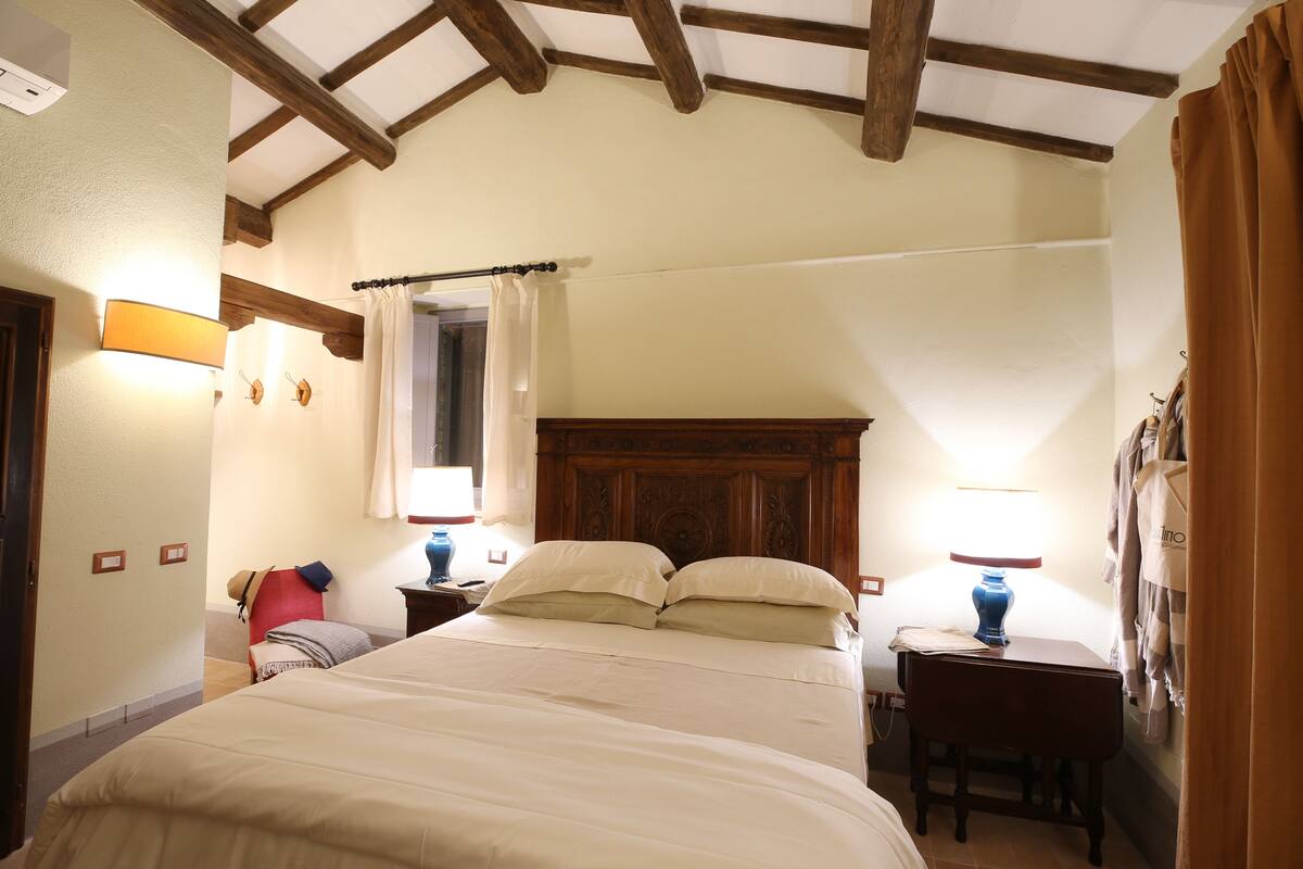 A bedroom with a large bed, two bedside tables with lamps, a wooden headboard, and a ceiling with exposed beams.