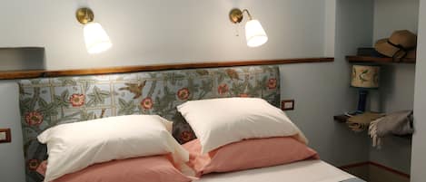 A bed with two pillows, a headboard with floral wallpaper, and two wall-mounted lights.