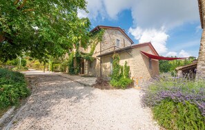 A stone building with a gravel driveway, surrounded by greenery and lavender plants. - Casa Minotti (Gubbio)