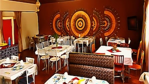 Un comedor con varias mesas y sillas, un adorno mural estampado y una puerta roja.