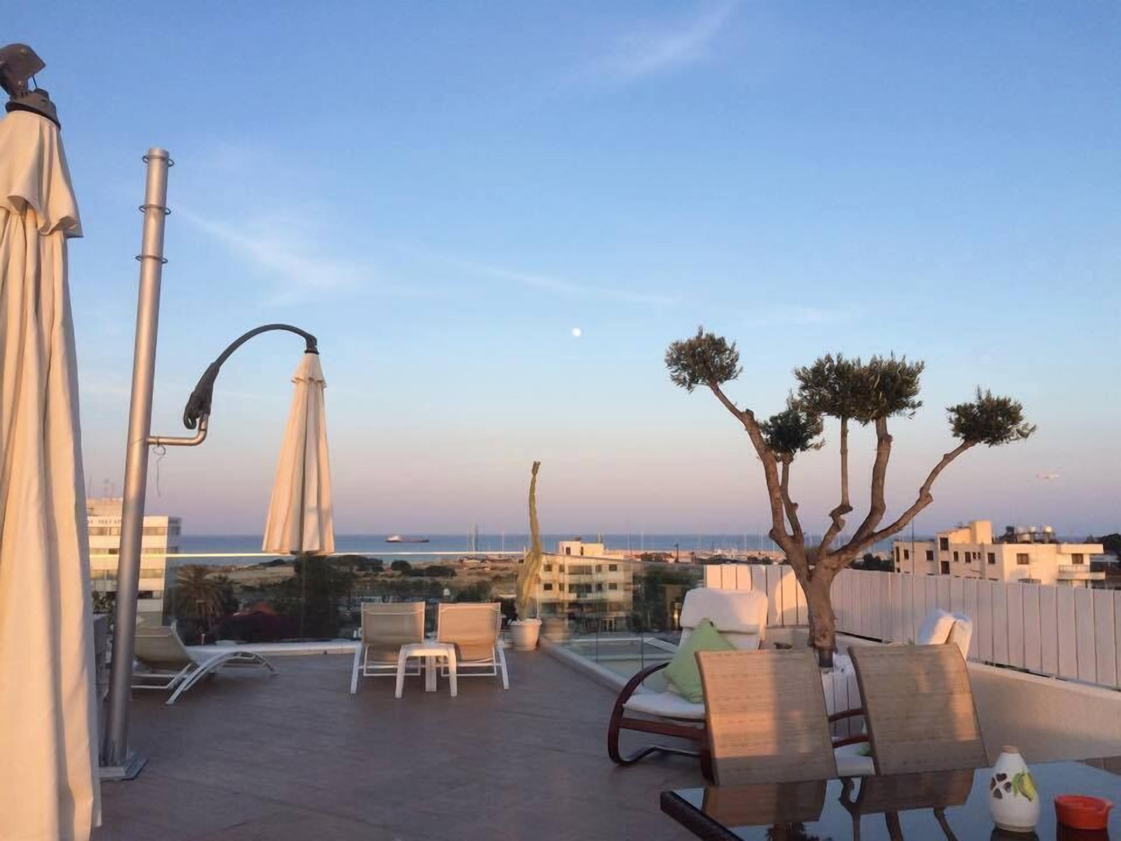 Una terraza en la azotea con mobiliario exterior, vistas al mar y un árbol singular.
