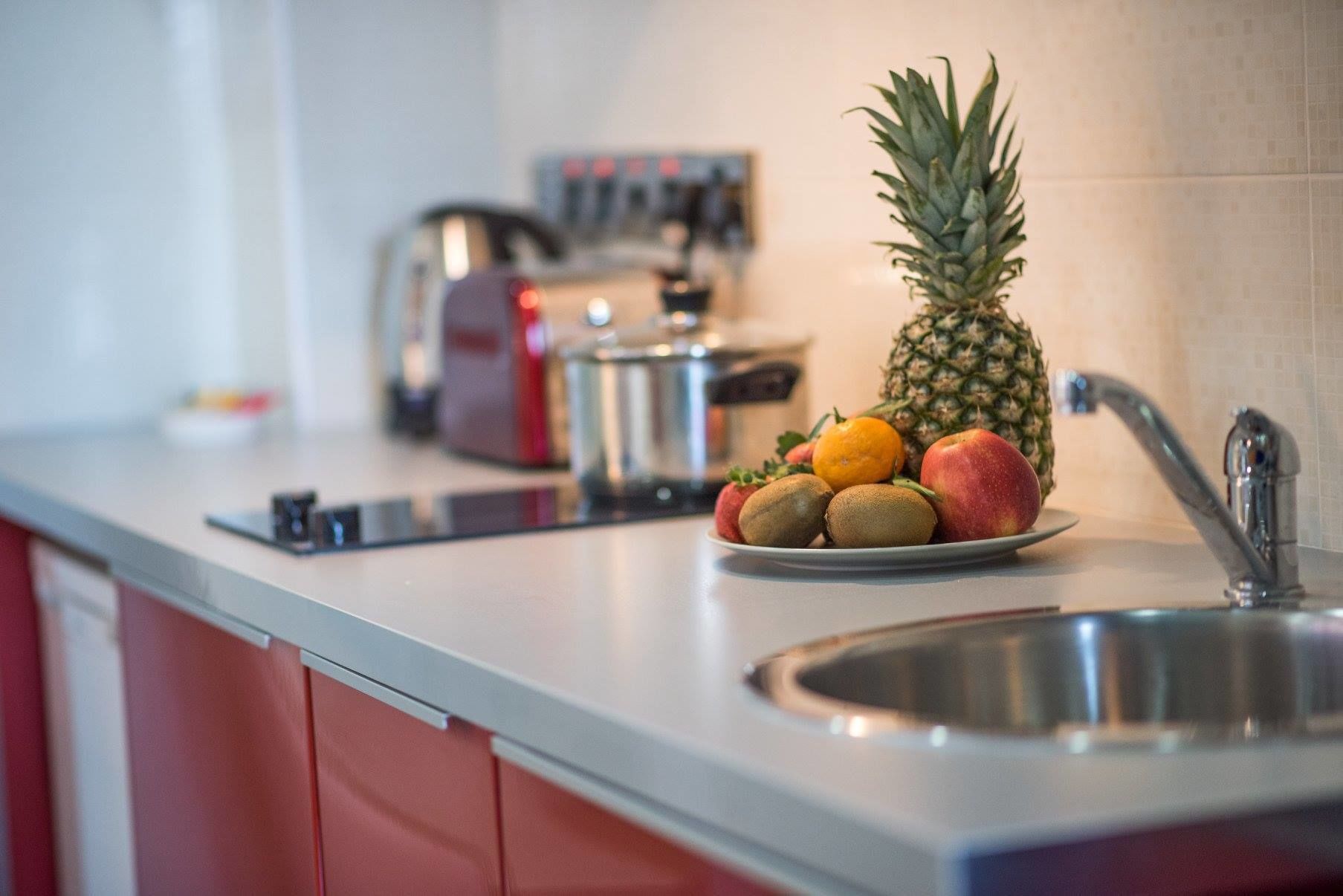 A kitchen counter with a plate of fruits, a pineapple, and a coffee maker.