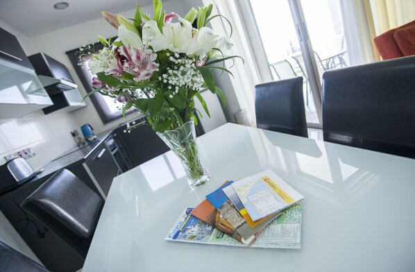 A modern hotel room with a glass dining table, a vase of flowers, and a view of the city through the window.