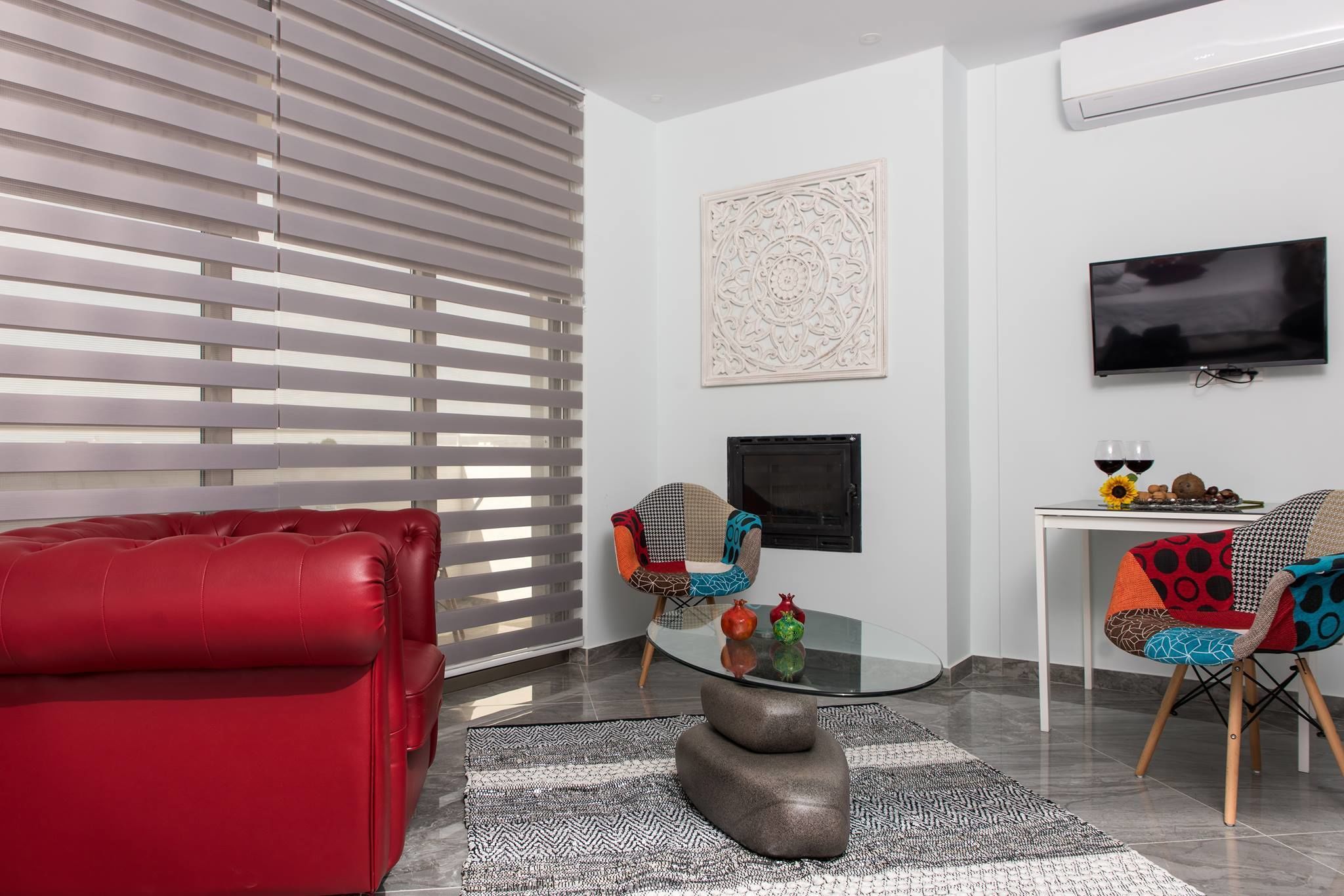 Un salon moderne avec un canapé rouge, une table basse en verre et deux fauteuils à motifs.