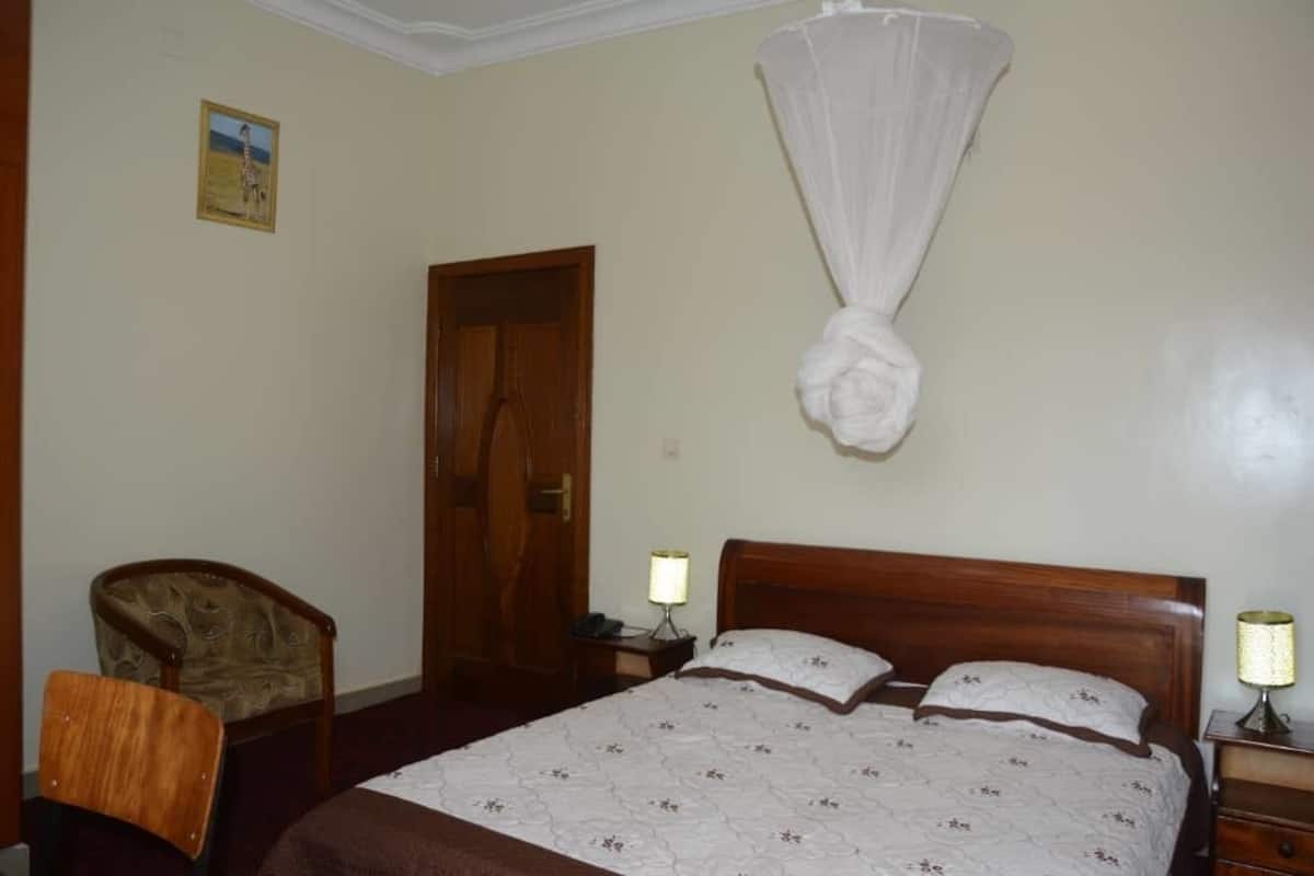 Une chambre d’hôtel avec un lit, une chaise, une table de chevet avec une lampe et une porte.