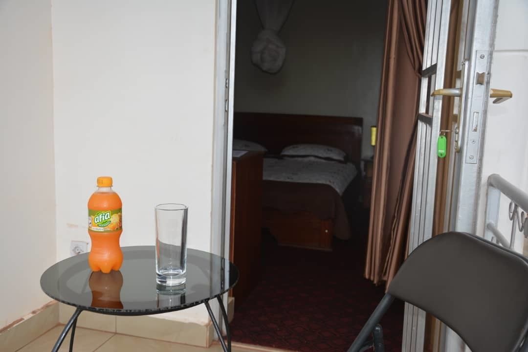 A small room with a bed, a chair, a table with a bottle and glass, and a door with a lock.