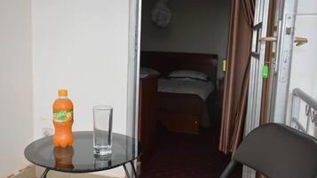 A small room with a bed, a chair, a table with a bottle and glass, and a door with a lock.