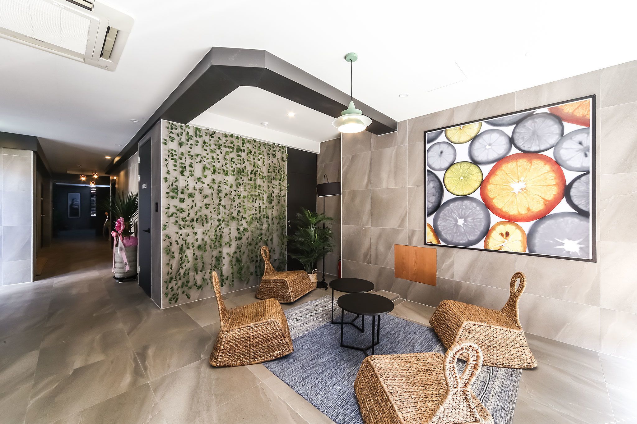 A modern lobby with a high ceiling, a large wall-mounted artwork of citrus slices, and a seating area with woven chairs and a small table.