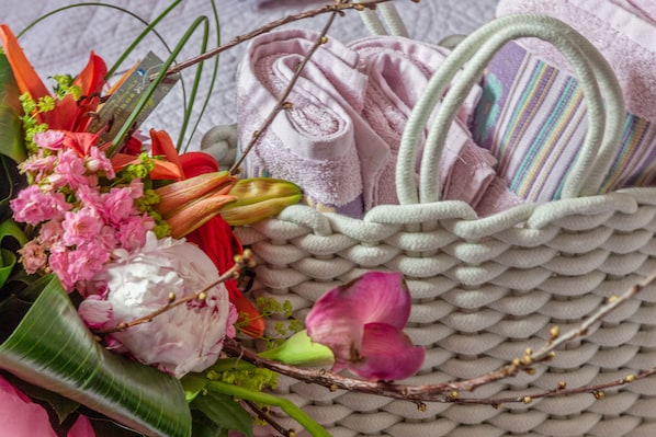 Una cesta tejida llena de flores rosadas y una toalla enrollada.
