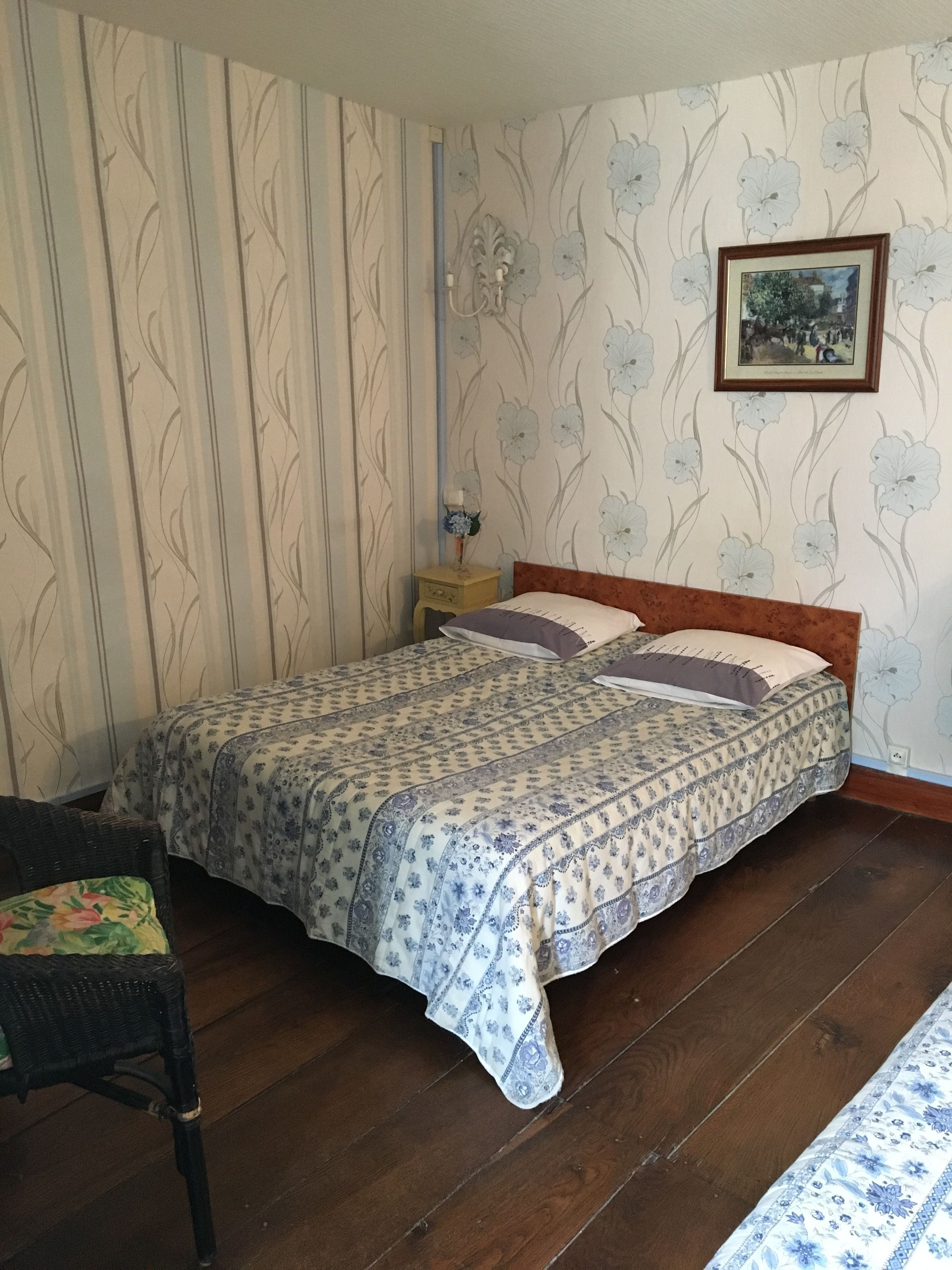 Un dormitorio con una cama, una mesita de noche, una silla y un cuadro en la pared.